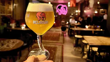 Hand hält Delirium-Bierglas in gemütlicher Bar-Atmosphäre.