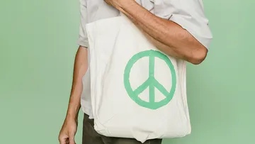 Man is wearing a cloth bag with peace symbol against a green background.