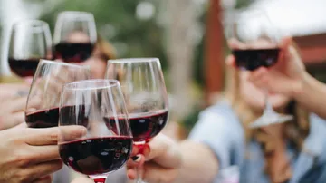 Gläser mit Rotwein stoßen zusammen in fröhlicher Atmosphäre.