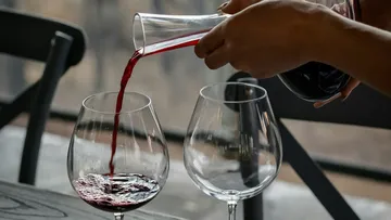 Ein Glas wird mit Rotwein aus einem Krug gefüllt.