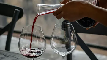 Ein Glas wird mit Rotwein aus einer Karaffe gefüllt.