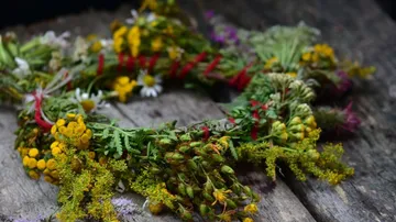 Blumenkranz liegt auf Holzoberfläche, umgeben von Natur.