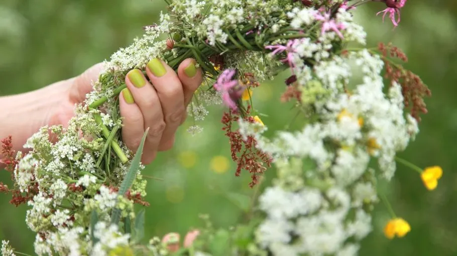 Hand holds wreath made from various flowers and herbs.