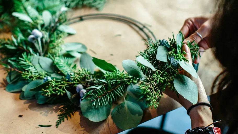 Young woman creates a wreath from green plants.