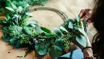 Person creates a wreath of green leaves and branches.