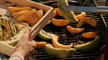 Grilled vegetables are placed on the grill from a wooden board.