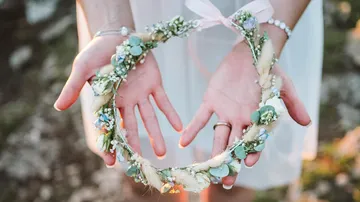 Hands hold a wreath of flowers in a natural setting.