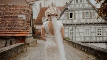 Bride in dress with hat walks on cobblestone street.