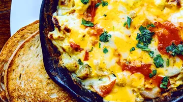 Eisenpfanne mit geschmolzenem Käse und geröstetem Brot.