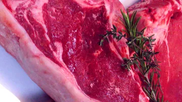 A piece of raw meat with fresh herbs next to it.