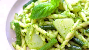 Nudeln mit Pesto, Gemüse und frischem Basilikum auf einem Teller.