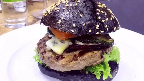 Schwarzer Burger mit Gemüse und einem Salatblatt.