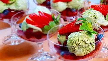 Eisbecher mit Früchten, dekoriert mit Erdbeeren und Minze.
