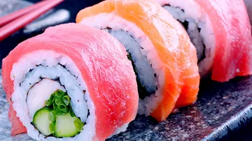 Bunte Sushi-Rollen liegen auf einem dunklen Teller.