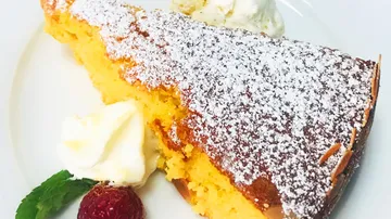 Piece of cake served with powdered sugar, cream and raspberry.