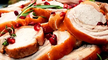 Sliced meat decorated with pomegranate seeds and herbs.