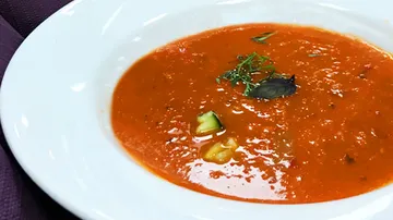 Red soup mixed with vegetables served on a white plate.