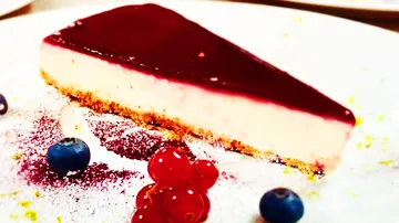 Käsekuchenstück mit Beerensoße auf einem weißen Teller.