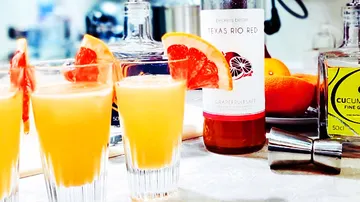 Cocktails in glasses with pieces of grapefruit on table.