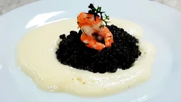 Schwarzer Reis mit Garnelen auf einer weißen Sauce.