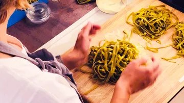 Grüne Pasta wird auf einem Holzbrett geformt.