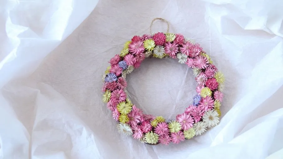 Colourful wreath of flowers hangs on white, crumpled paper.