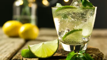 Glass with drink, ice and lime, wooden background, fresh herbs.