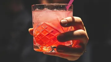 A glass of pink drink is held.