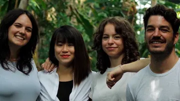 Four people are smiling in a green, natural setting.