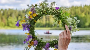 Wreath of flowers is being held; calm lake and forest view in the background.