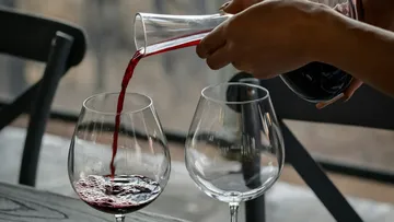 A carafe pours red wine into wine glasses.
