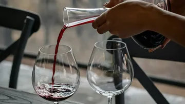 Eine Person gießt Rotwein in ein Weinglas.