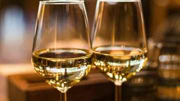 Two glasses of white wine reflect light in a room.