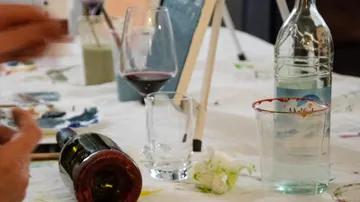 Tisch mit Weinglas, Flasche und Malutensilien.