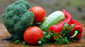 Green vegetables and fresh fruit lie on the wooden surface.