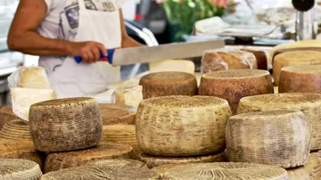 Käse wird von Verkäufer an einem Markttisch geschnitten.