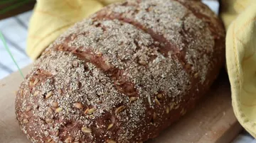 A loaf of bread lies on a wooden board surrounded by cloths.