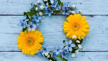 Blumenkranz aus gelben und blauen Blumen auf Holz.