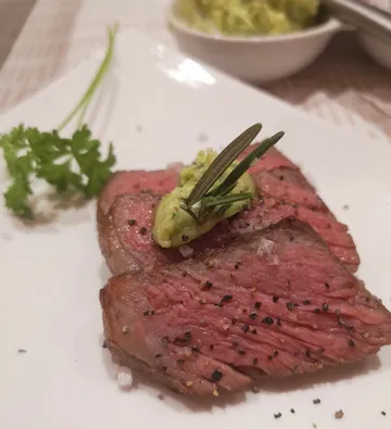 Gegrilltes Steak mit Guacamole und Kräutern auf weißem Teller.