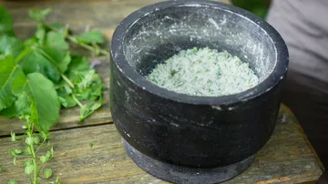Mortar with crushed herbs on a wooden table.