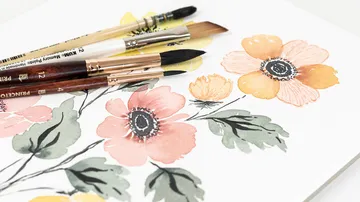 Pinsel liegen auf einem Aquarellbild mit Blumenmotiven.