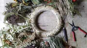 A straw ring is surrounded by fresh dried flowers and tools.