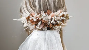 Wreath of flowers adorns long hair in front of a veil.