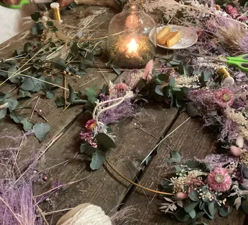 Blumenkranz wird gefertigt, umgeben von Naturmaterialien und Licht.