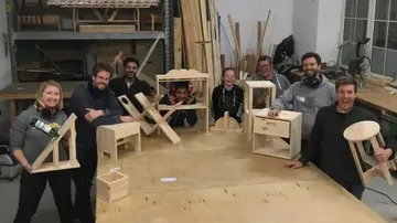 Group of people showing homemade furniture in a workshop.