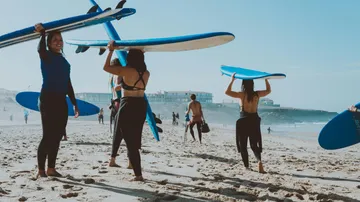 Surfer tragen Bretter am Strand unter blauem Himmel.