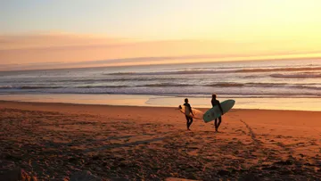 Zwei Surfer gehen am Strand bei Sonnenuntergang.
