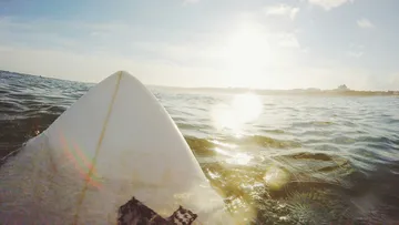 Surfbrett auf dem Wasser, sonniger Himmel, ruhige Wellen.