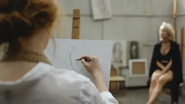 Künstlerin zeichnet Aktmodell in einem Atelier.