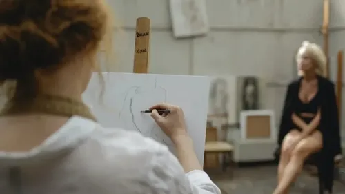 Eine Künstlerin zeichnet eine sitzende weibliche Aktfigur in einem Atelier.